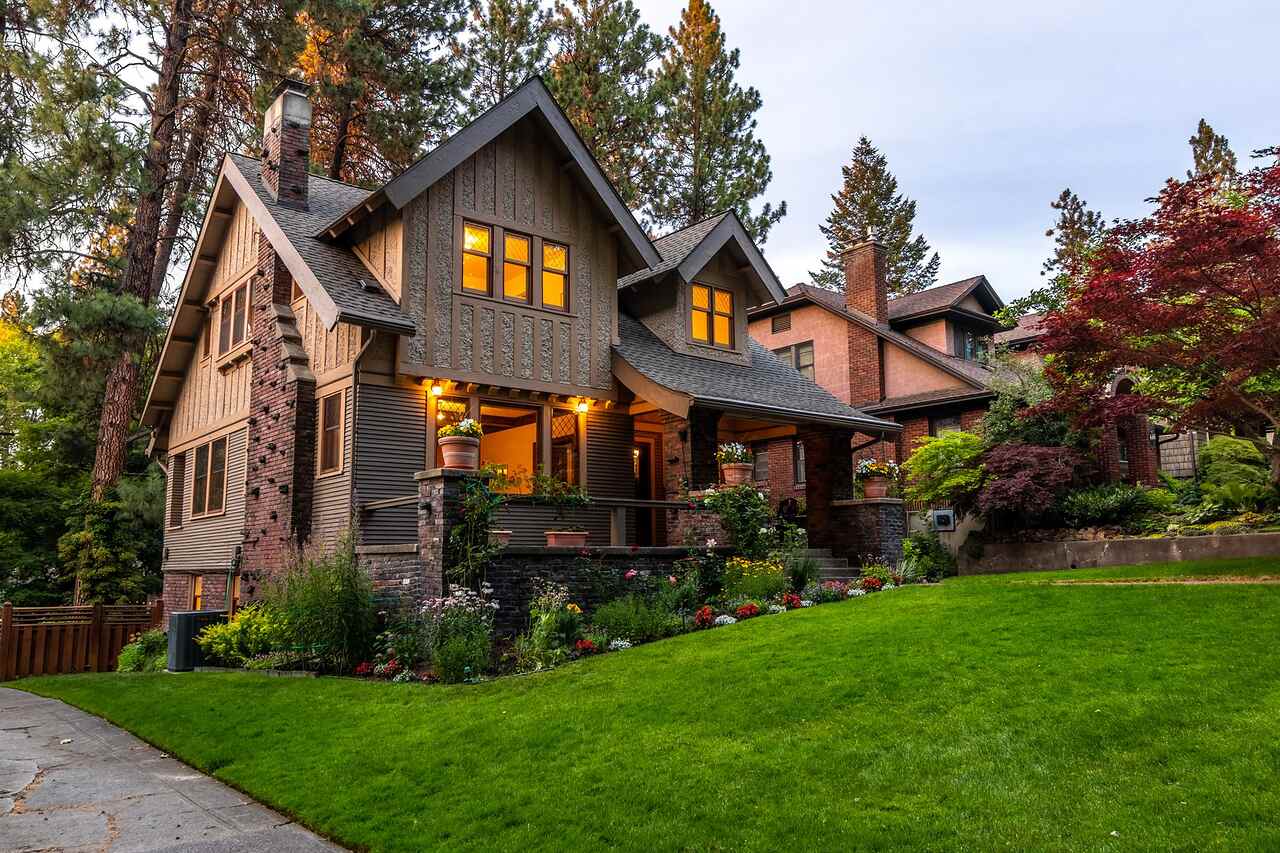 An older house lit from within at twilight behind a densely planted front garden