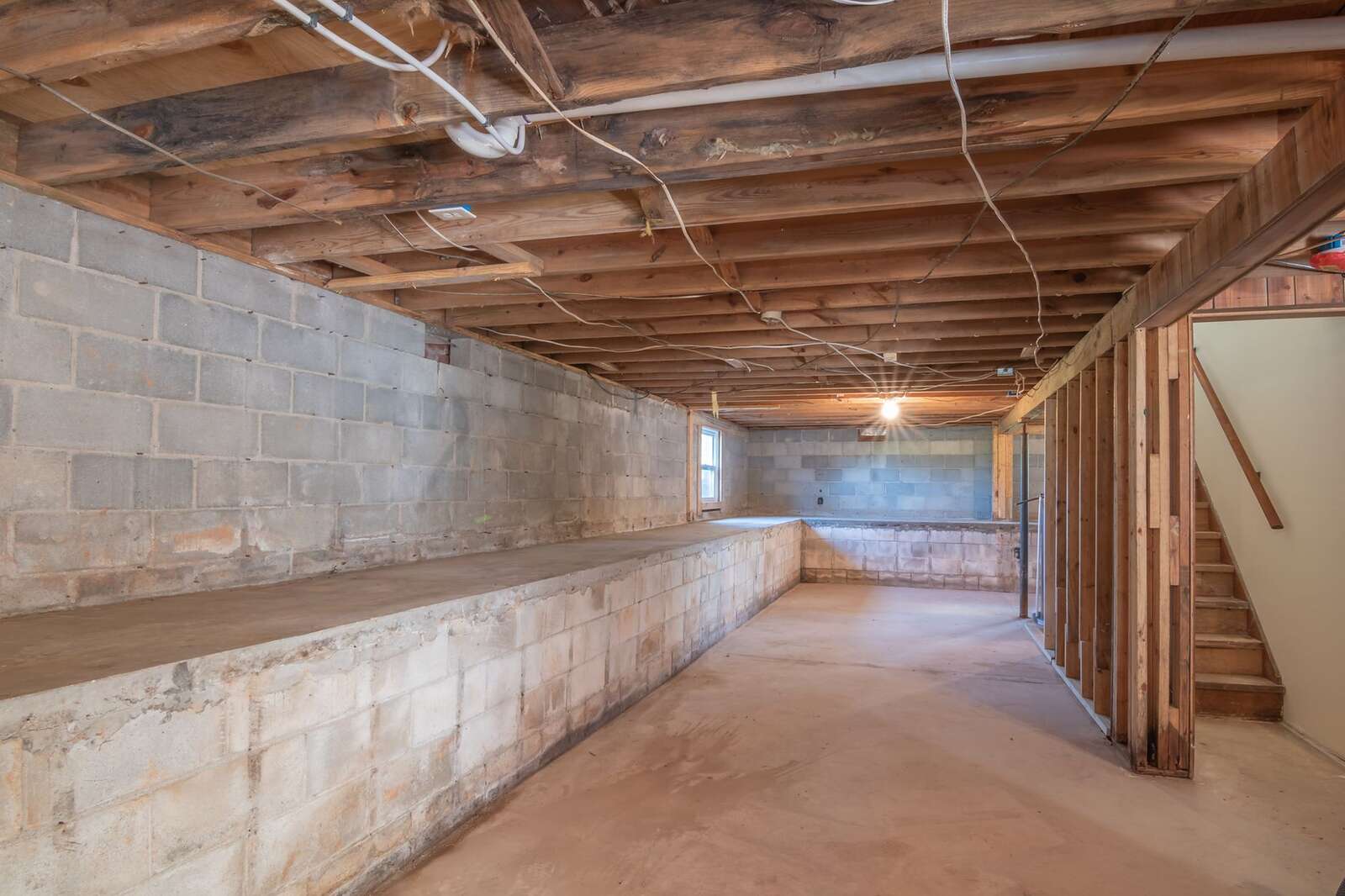 An unfinished under-floor space with exposed wooden beams, block walls and a concrete floor