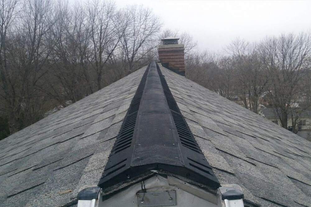 The ridge vent along the peak of a shingle roof seen from ladder height