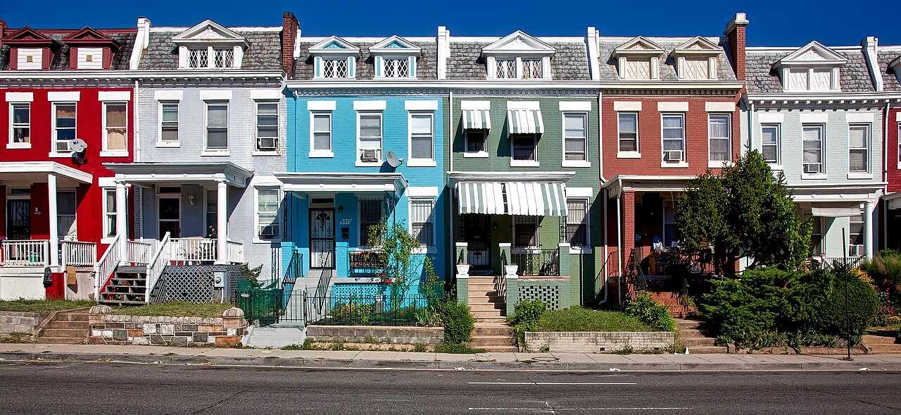 A row of narrow attached houses standing close to the sidewalk on a tight street