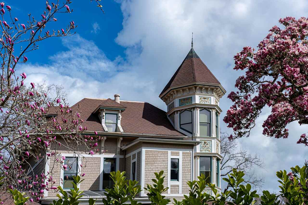 A Victorian house with a turret and a complicated roofline under spring blossom